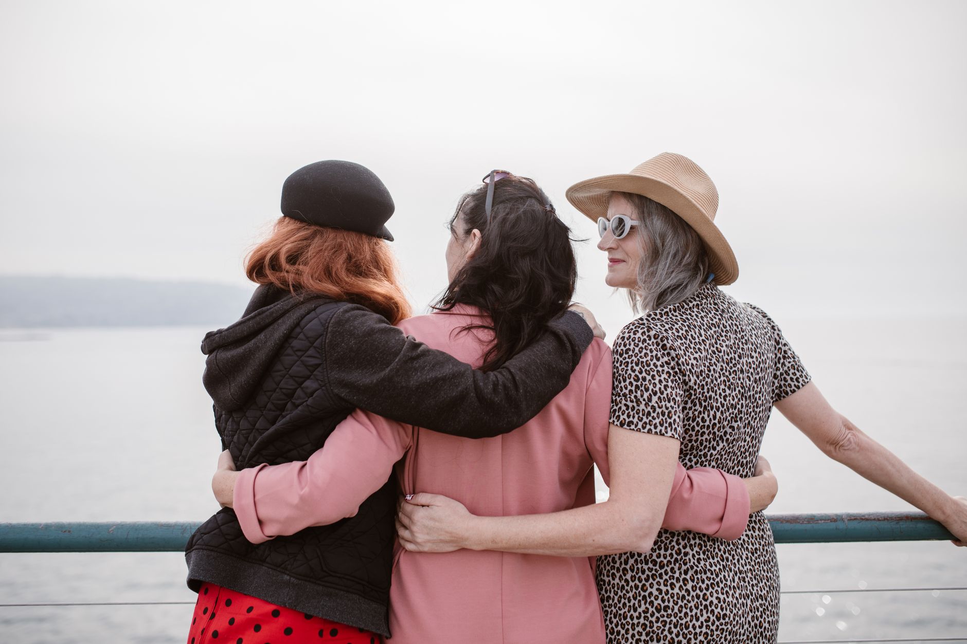 back view of girlfriends holding each other while standing on metal barrier